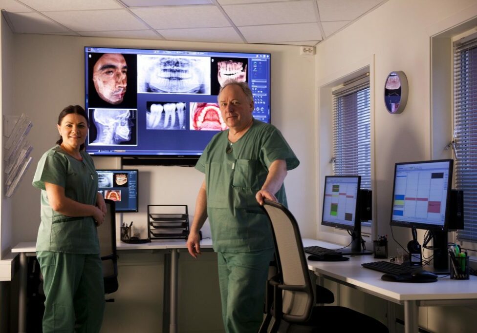Kontrollrommet hos Tromsø Tannkirurgi og narkosesenter er godt utstyrt slik at ekspertene kan forberede seg godt før hver behandling. På bildet ser du en storskjerm, tre vanlige dataskjermer og to personer som studerer ulike bilder - både rødtgen og vanlige bilder. 